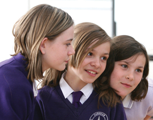 Three young teenagers in school uniform look at something out-of-shot